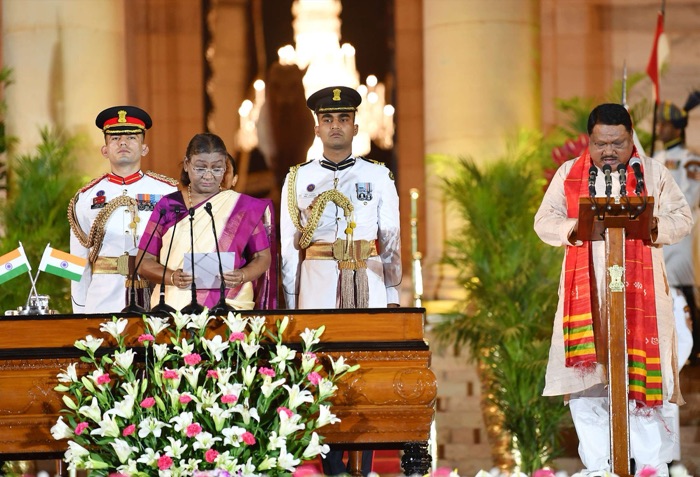 Jual Oram at a lectern taking the oath of office, with President Droupadi Murmu seated at left